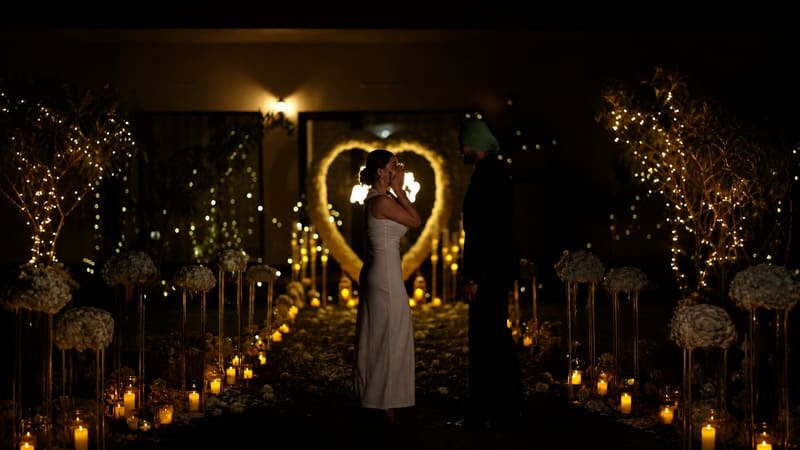 Couple under a glowing heart arch on a candlelit aisle
